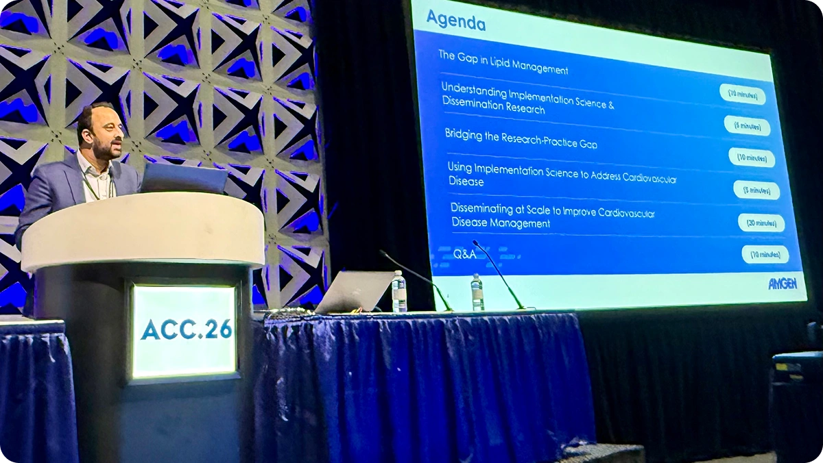 Presenter at the ACC26 podium beside a screen showing the session agenda