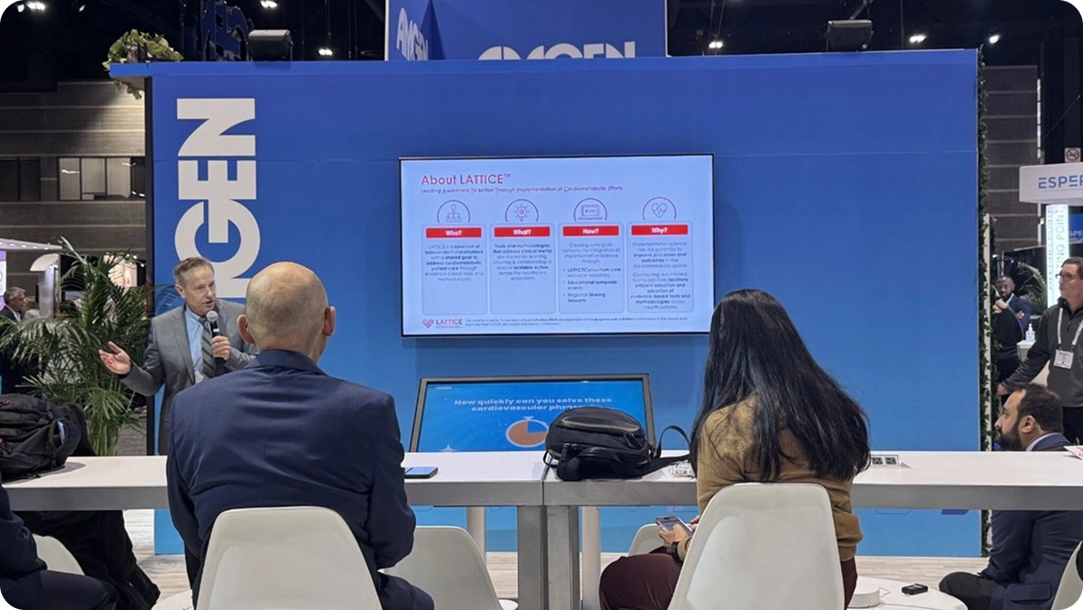 Presenter showing an "About LATTICE" overview slide to a seated audience at the Amgen exhibit booth